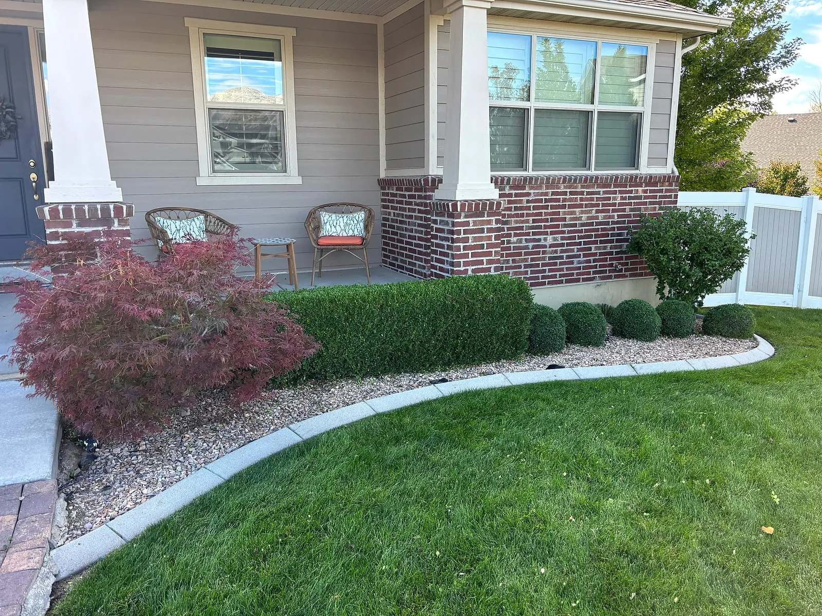 A front porch with a squared boxwood hedge, a red Japanese maple and a curved concrete border around a green lawn, cared for by Taylor’d Lawn Care