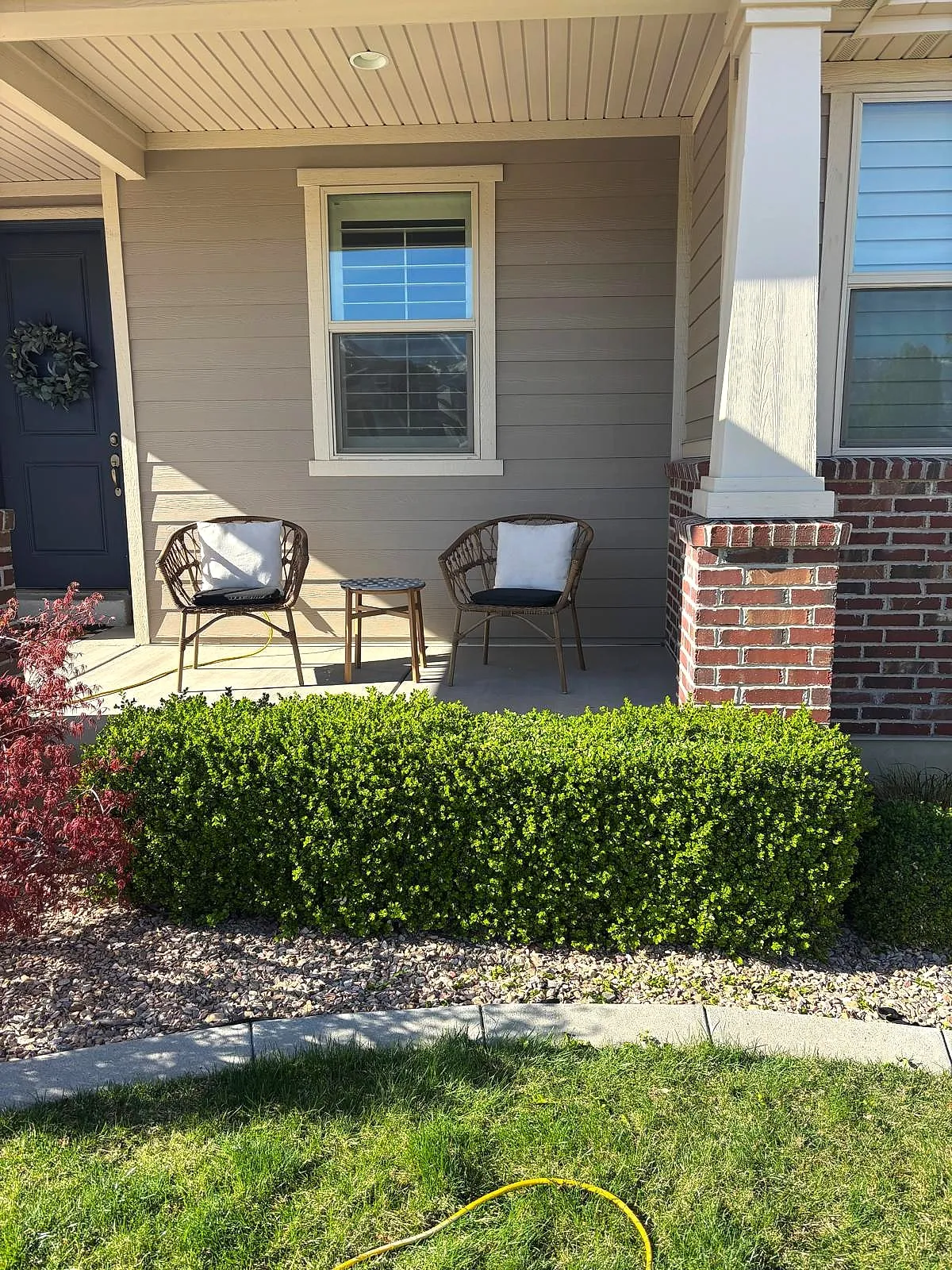 A boxwood hedge trimmed flat and square in front of a porch, trimmed by Taylor’d Lawn Care